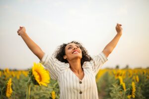 Frau steht im Sonnenblumenfeld und streckt Arme vor Freude nach Oben